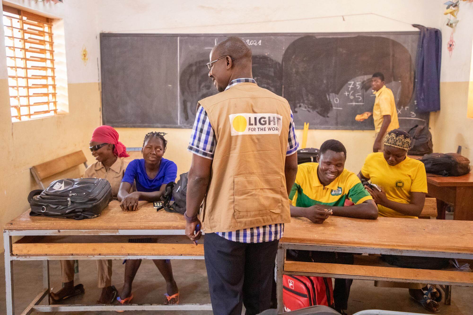 Image of a teacher with a Light for the World jacket and students with visual impairments in a classroom in Burkina Faso. Hundreds of students with visual impairments in Burkina Faso have been provided with assistive technology devices under a project run by Light for the World, UN-ABPAM, Daisy Consortium and Benetech.