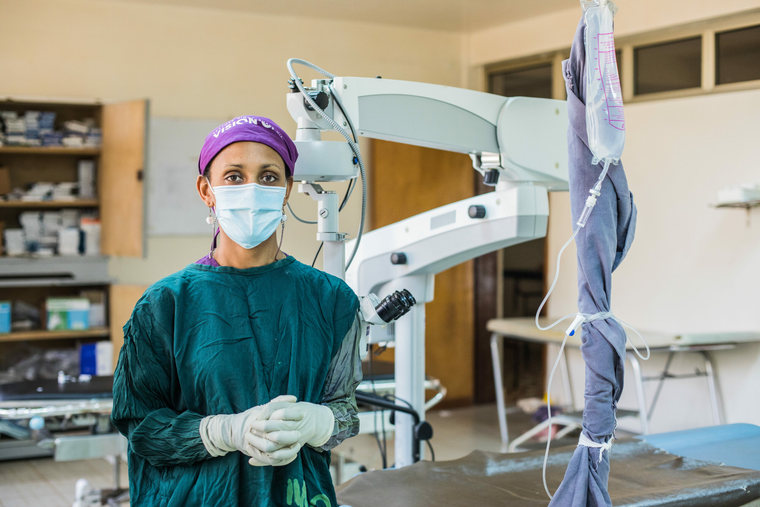 Dr. Kumelle Tollosa is wearing a medical mask and protective scrubs and gloves. She stands in front of surgical equipment.