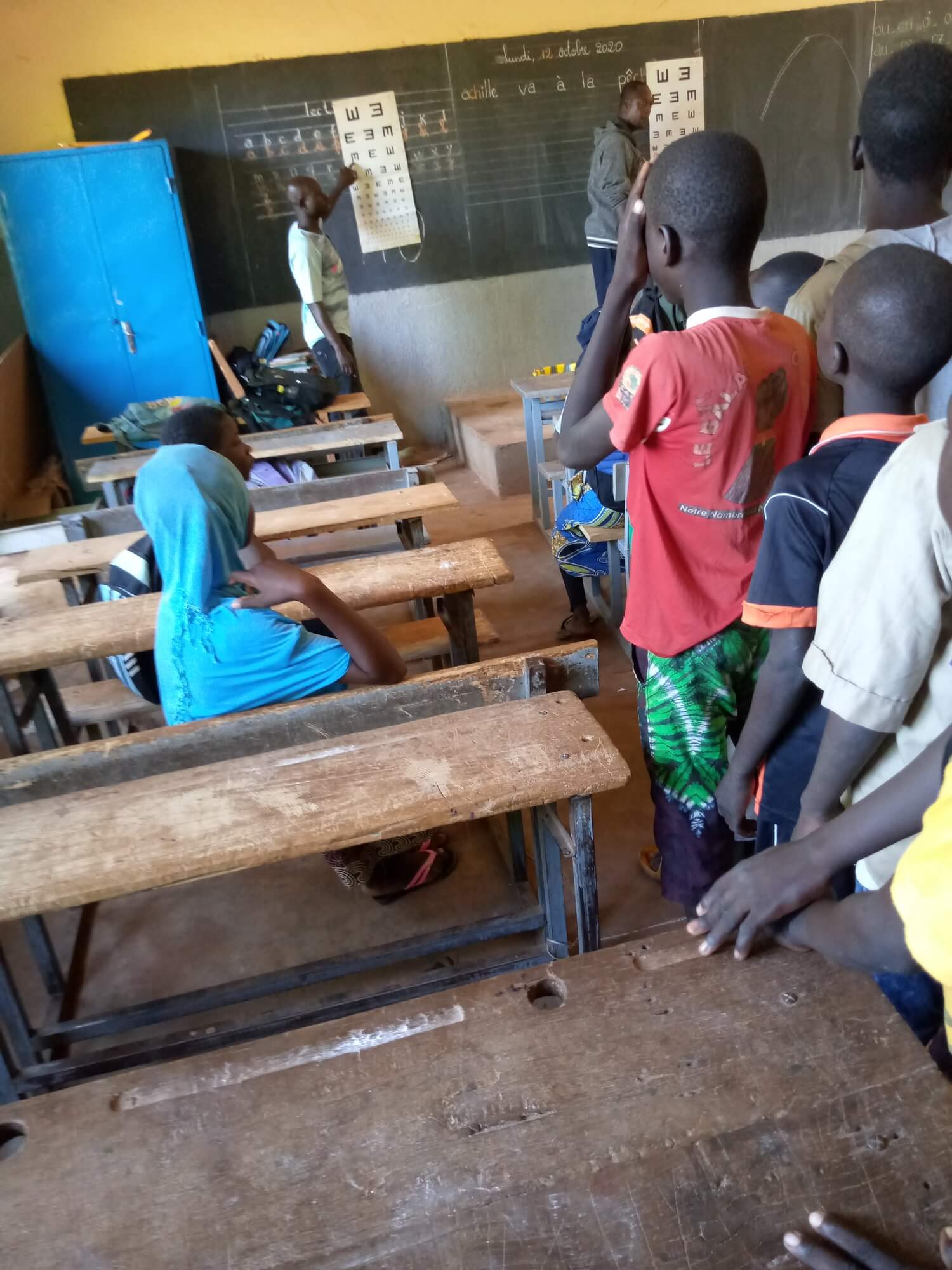 Images of pupils in a classroom lining up for an eye test.