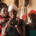 Image of three women who participated in the project: Overcoming Barriers to Food Security: A photo narrative by people with disabilities. The woman in the middle of the three holds a camera.