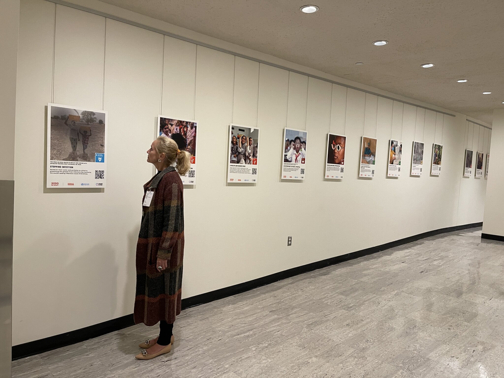 Herta Kriegner looks at a exhibition of photos. She is wearing a long coat and has her hair tied back.