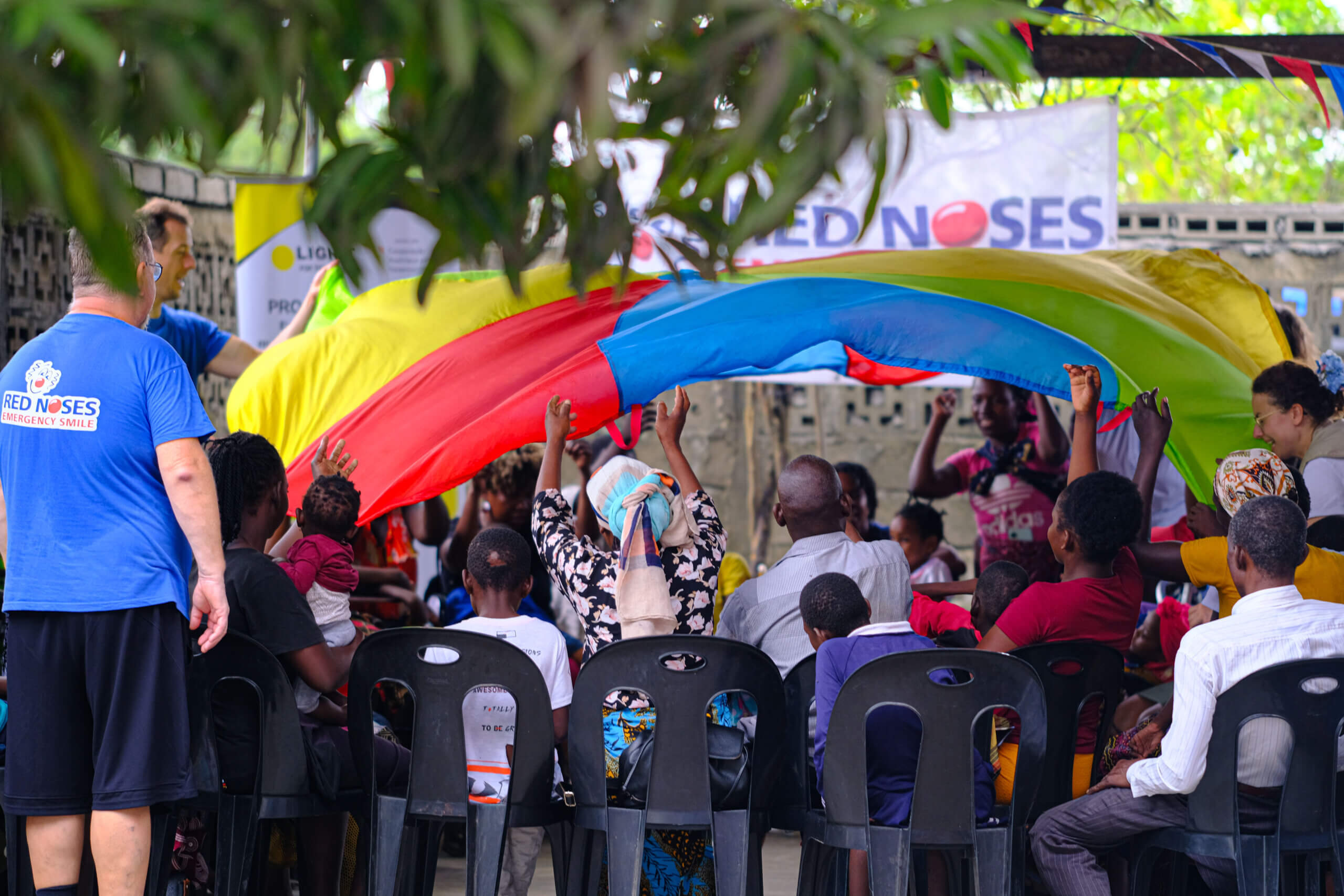 People are holding a giant multi-coloured fabric. They have their hands in the air and the mood is celebratory,