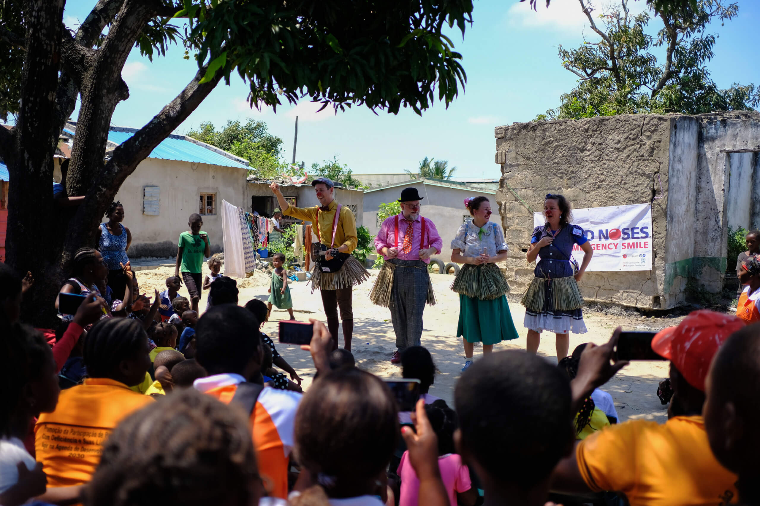 Representing one of the good news stories of 2023, four people dressed as clowns, smiling and singing, are performing in front of a crowd. Working to break down stereotypes.