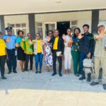 A group of several people stand together, some wearing yellow 