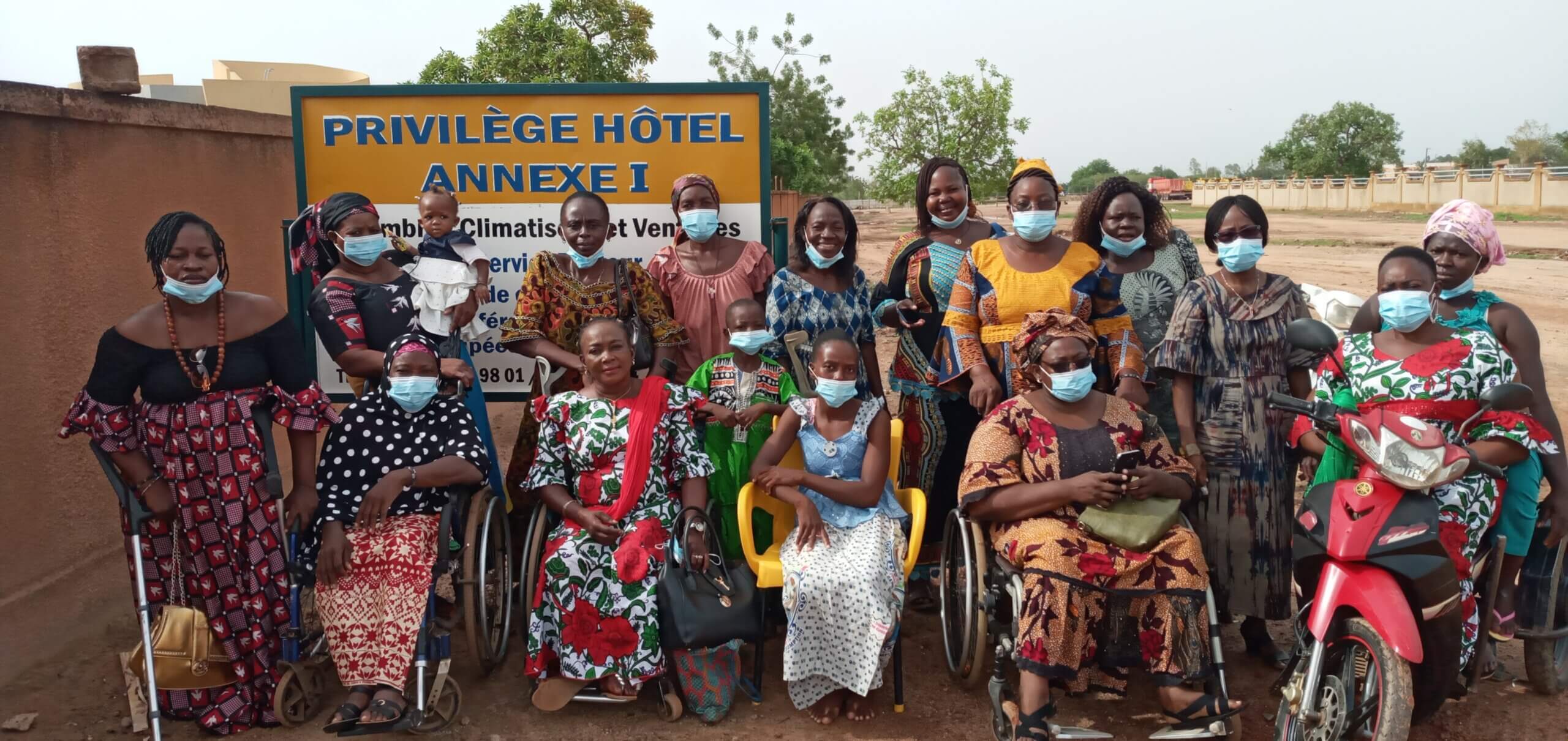 Celebrating International Day of People with Disabilities. The image shows the National Union of Women with Disabilities of Burkina Faso (UNAFEHB) outside. They are all wearing colourful clothes and face masks, some standing and some sitting in wheelchairs.