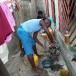 Pedro standing up against gender-based violence, subverting gender roles. He is wearing a blue top and trousers and helps to wash pots and pans.