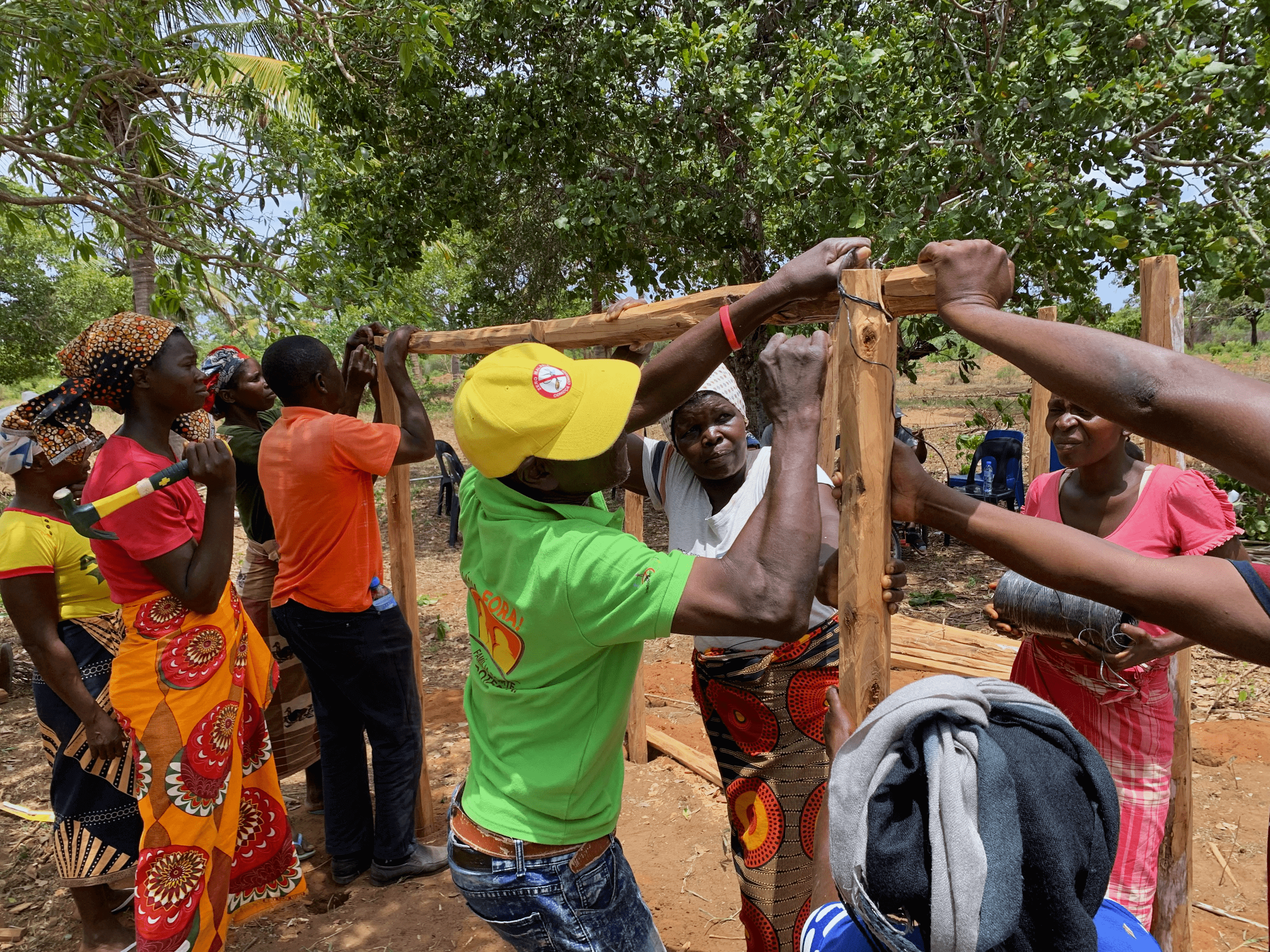 People with disabilities, facilitators, and design experts work together for climate action, building storage for grain and produce. Several people are building a wooden structure with three main poles.
