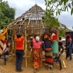 Climate action: farmers, facilitators, people with disabilities and design experts work together to build accessible storage for grain and produce. A group of people are building a small circular structure out of wood, with a pointed roof.