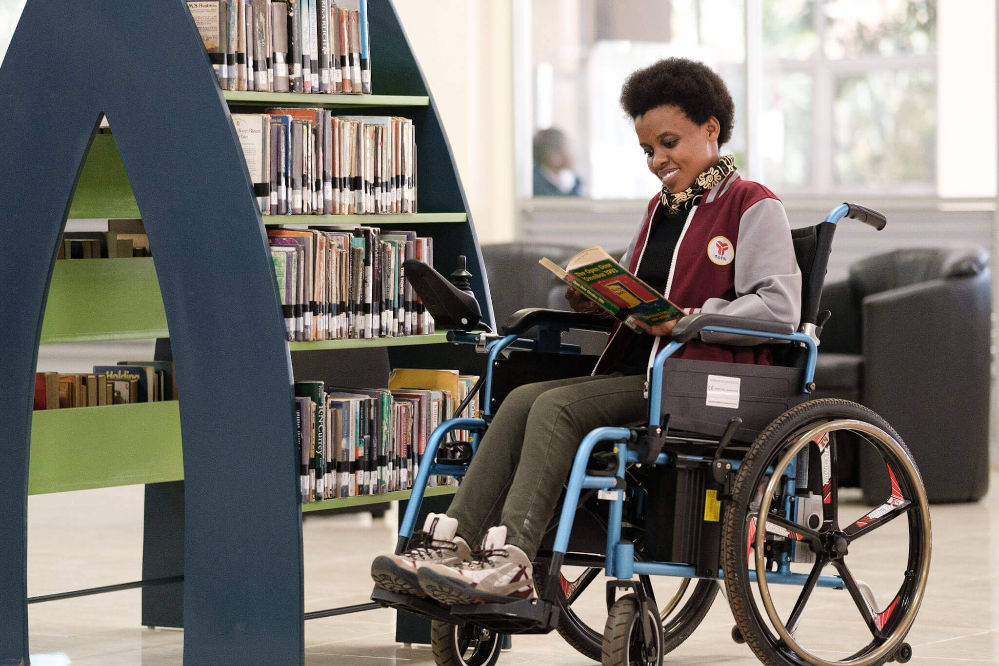 The image shows a woman in a wheelchair reading a book in a library. The CapAble project, which puts disability inclusion into action in higher education, has won a Zero Project Award.