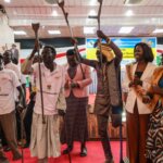 Several people from OPDs in South Sudan stand on stage, celebrating and dancing. Many wave crutches in the air.