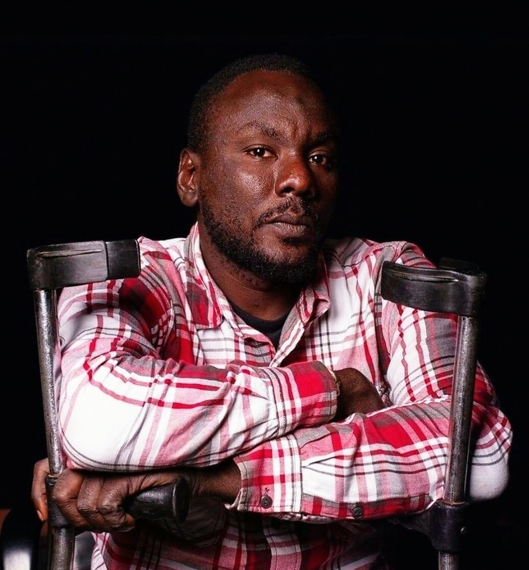 Bakary Diakite, from Senegal, who is one of the winners of the We Can Work storytelling competition. He received the Judges’ Honorary Award for a photo series called La Princessa. He is wearing a red and white checked shirt and has his arms folded as he looks at the camera. The background is black. Two crutches are visible either side of him.