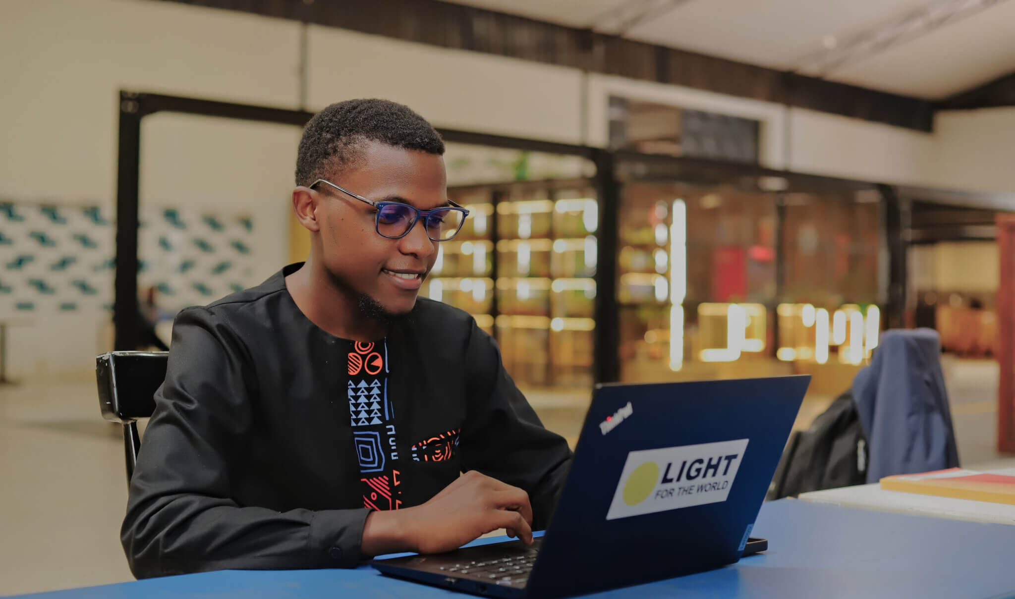 Isaac Muhumuza, one of the winners from Uganda. Isaac is smiling as he uses at a laptop.