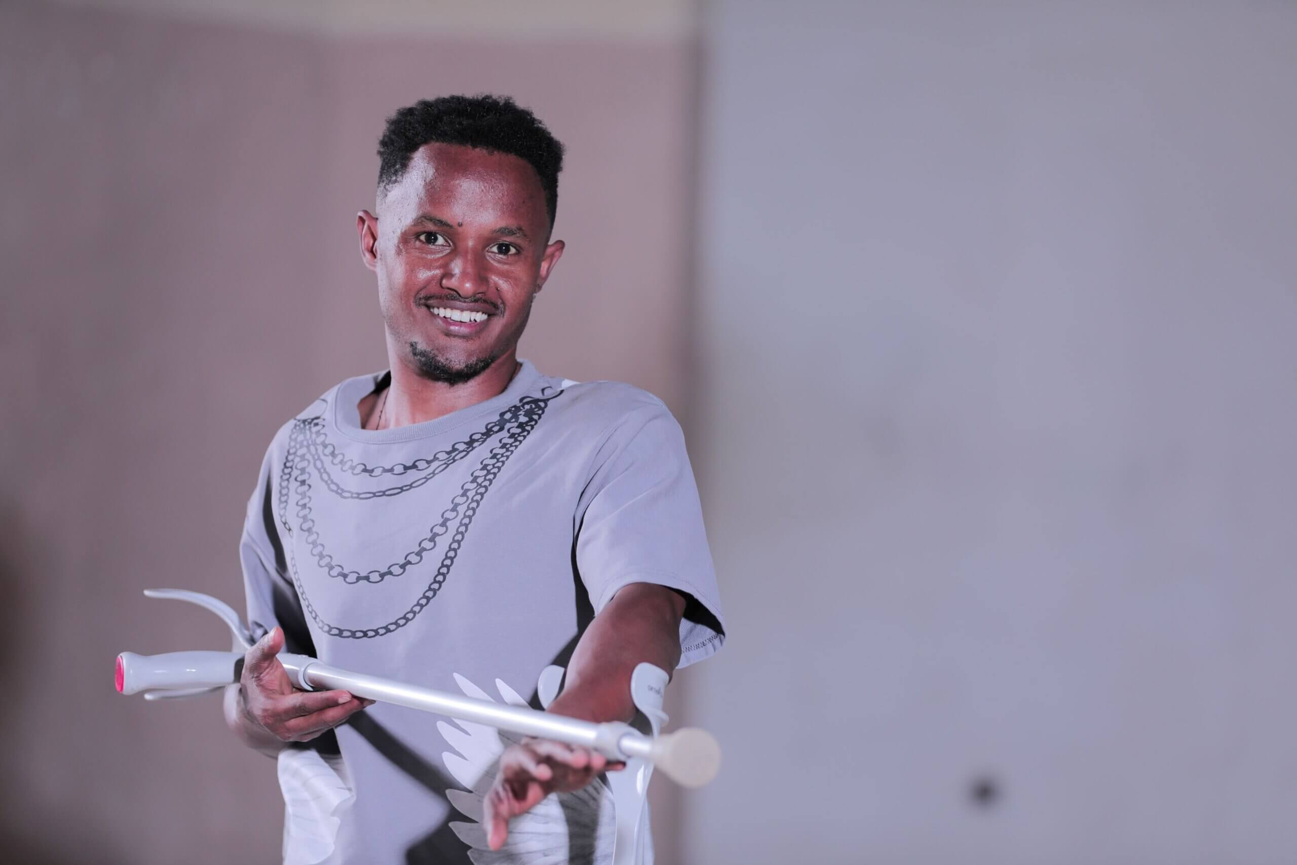 Amanuel Solomon, one of the winners of the We Can Work competition, for an interpretive dance short film highlighting resilience. He is wearing a grey t-shirt and smiling. He is holding a crutch pointed towards the camera.