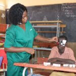 A nurse in green scrubs checks the eyes of a student in a classroom in Burkina Faso.