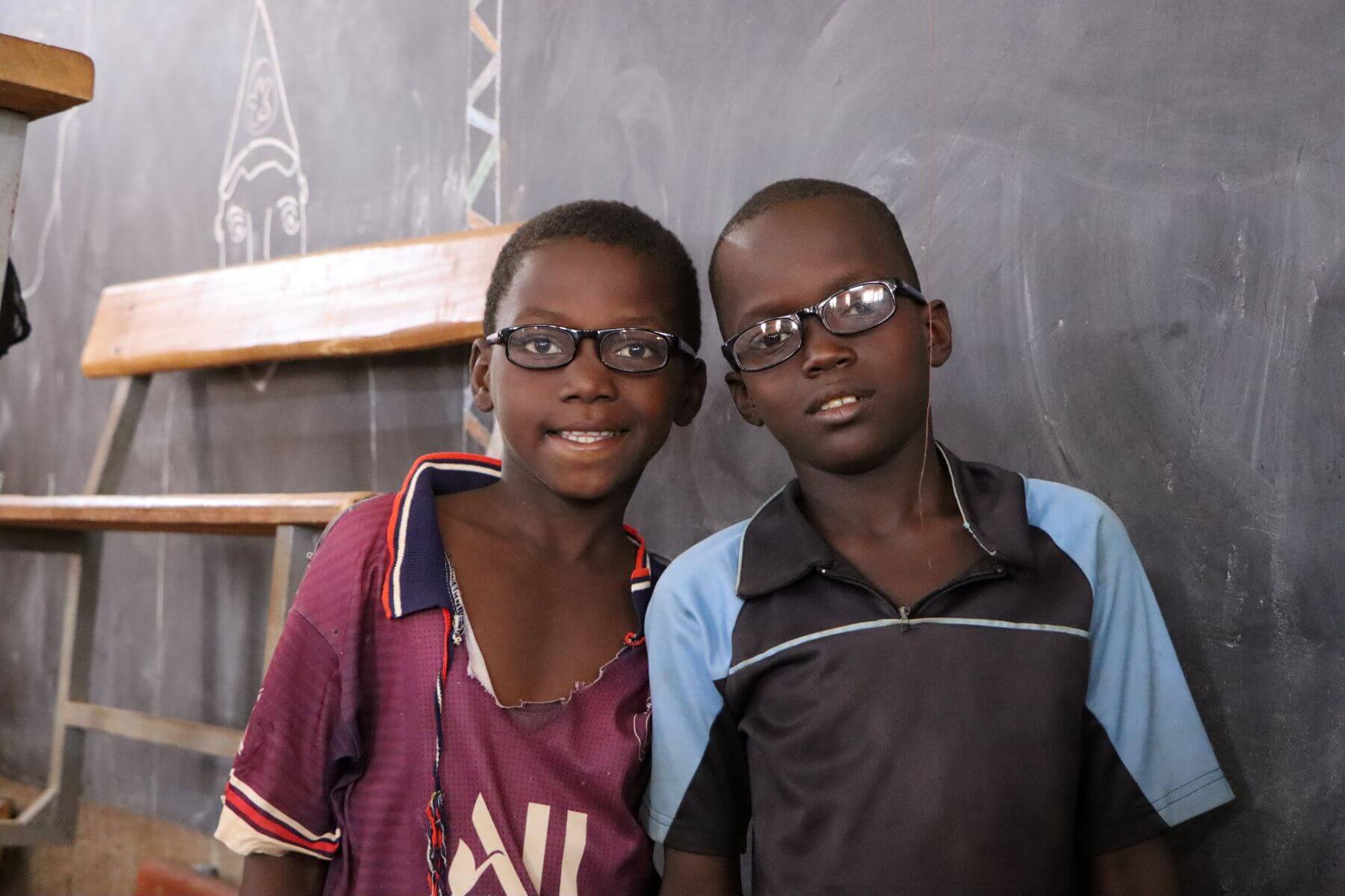 Two boys wearing glasses smile at the camera in a classroom in Burkina Faso.