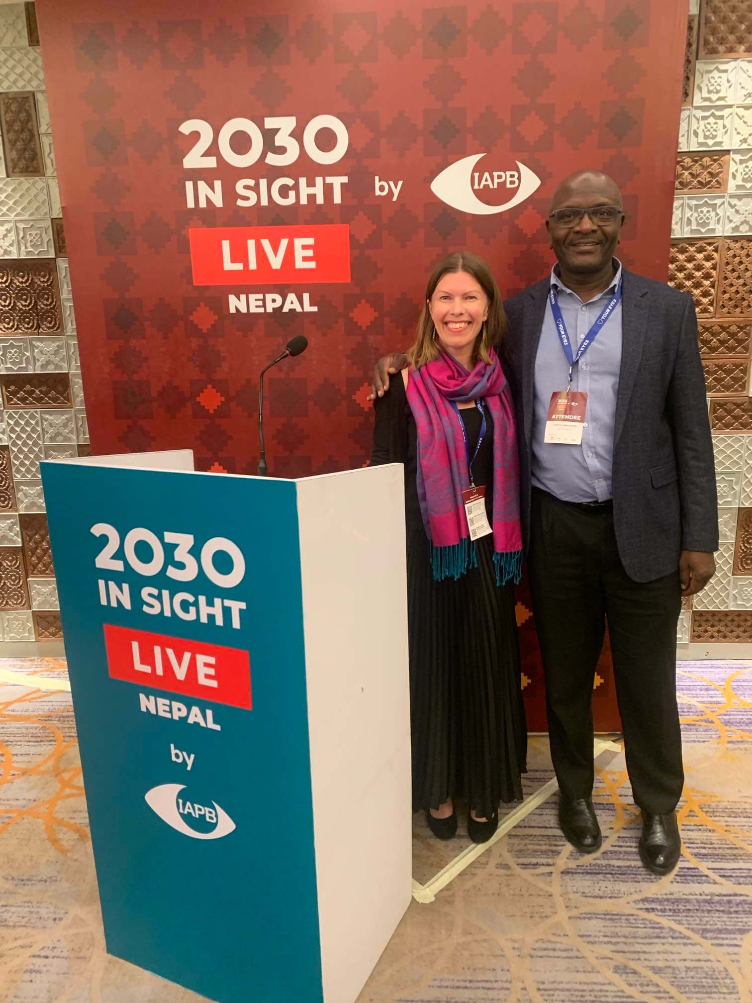 A European woman and African man at the Insight 2030 Summit. They are standing behind a small booth branded 2030 Insight and smiling at the camera.