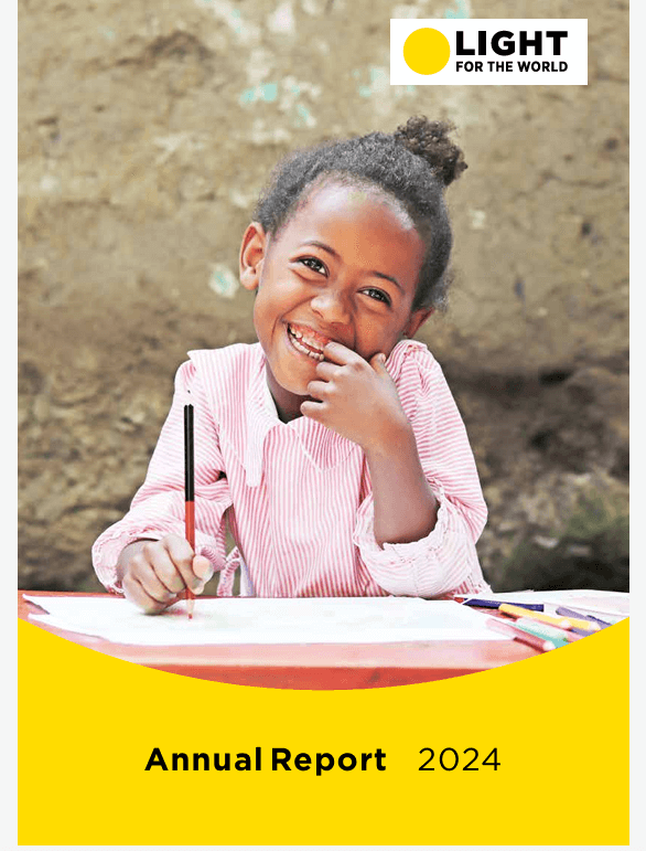 A young Ethiopian girl smiles while sitting at a desk outdoors. She wears a long-sleeved pink-and-white striped shirt and holds a red pencil above a white sheet of paper. The image is overlaid with the yellow and white Light for the World logo in the top-right corner and the words “Annual Report 2024” in black and yellow text at the bottom.
