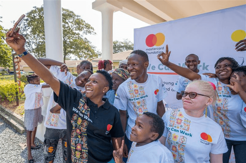 Racheal Njiru, a project manager in the We Can Work programme, takes a selife with some of the graduates. They are wearing “We Can Work” t-shirts with the Mastercard Foundation logo. Some of the graduates smile and make peace signs, creating a joyful, atmosphere.
