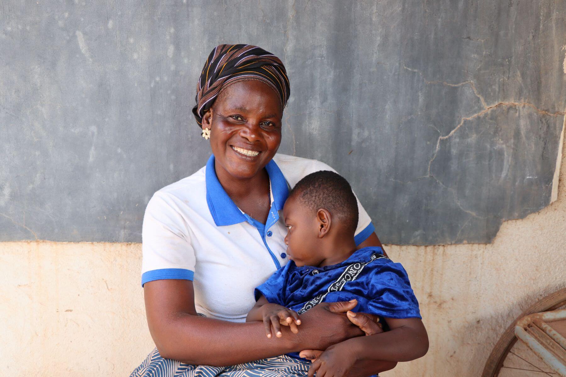 Songnaba Catherine holding her son Adonisa at a training for parents of children with cerebral palsy and intellectual disabilities in Burkina Faso. Catherine is smiling at the camera and Adonisa is looking away.
