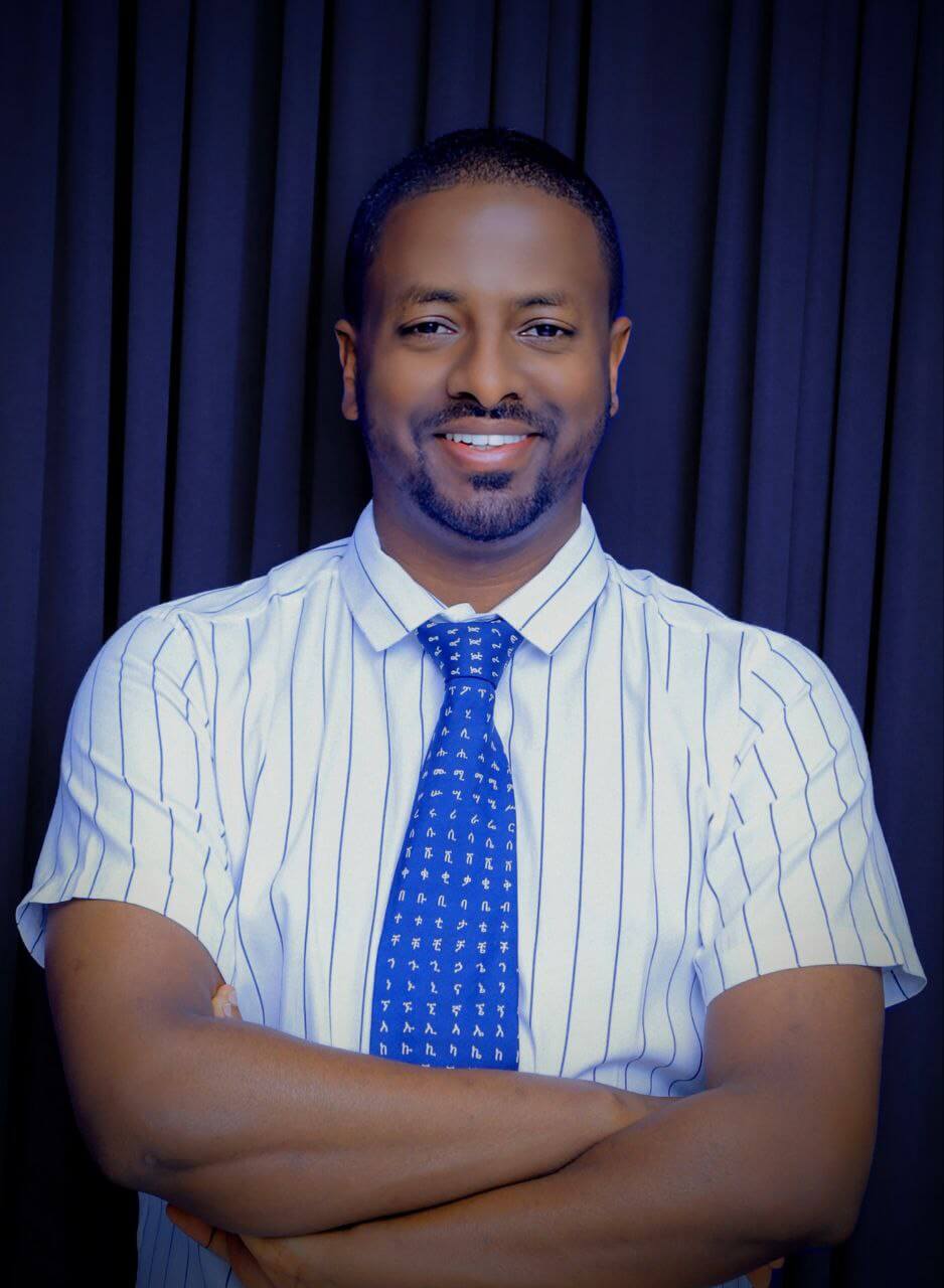 Dr Abebe wearing a white shirt and blue tie and smiling at the camera.