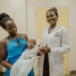 Dr Lusobya with Dylan Kigula and his mother, Joyce Namirembe. Dr Lusobya and Joyce are smiling and Joyce carries Dylan. Dr Lusobya is holding his hand.