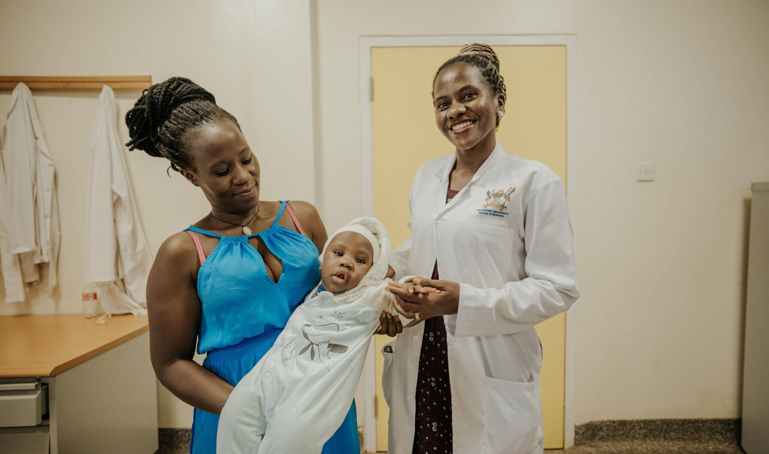 Dr Lusobya with Dylan Kigula and his mother, Joyce Namirembe. Dr Lusobya and Joyce are smiling and Joyce carries Dylan. Dr Lusobya is holding his hand.
