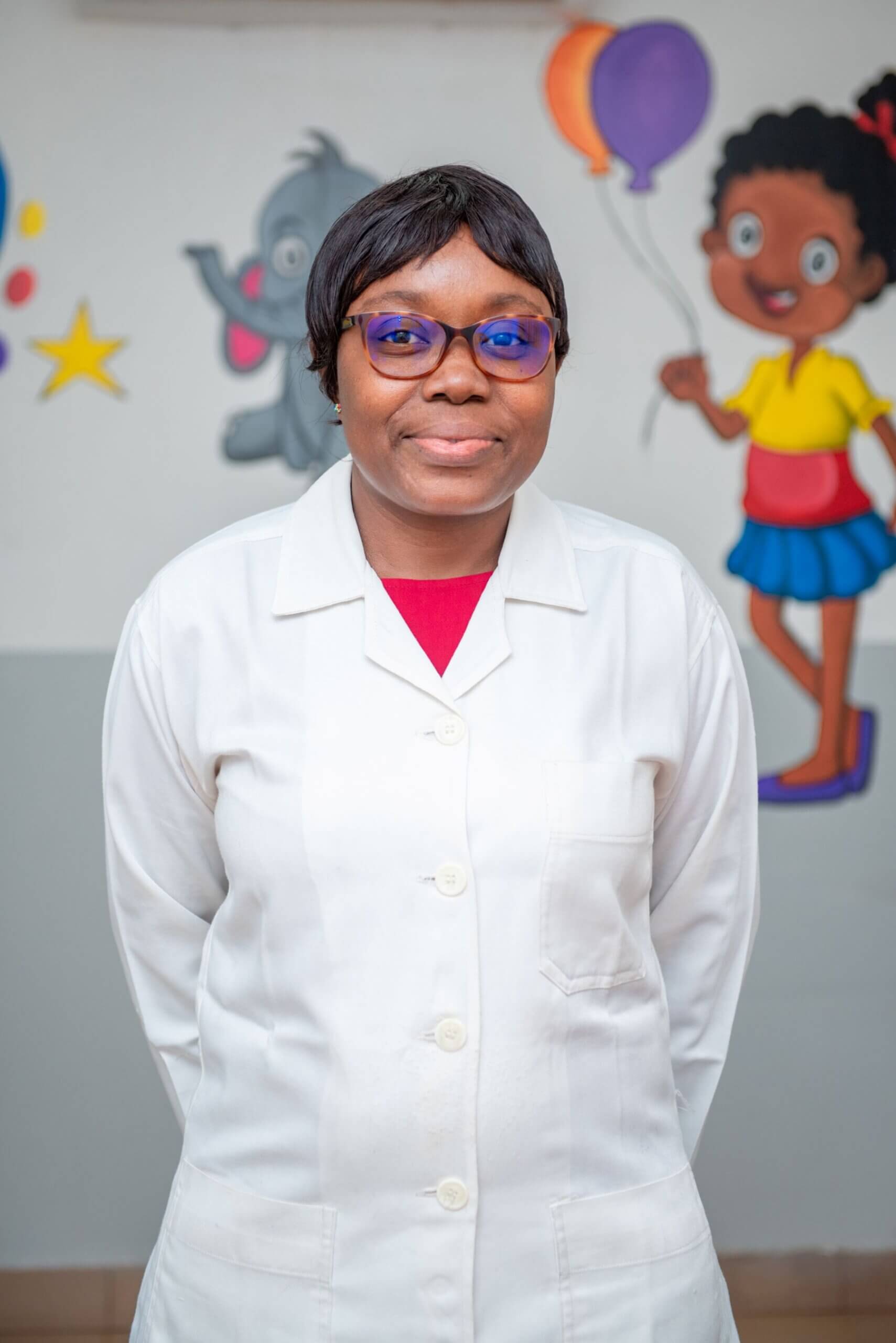 Dr Yaméogo wearing a white doctor's coat and smiling at the camera. Behind her is a wall with cartoon drawings on.