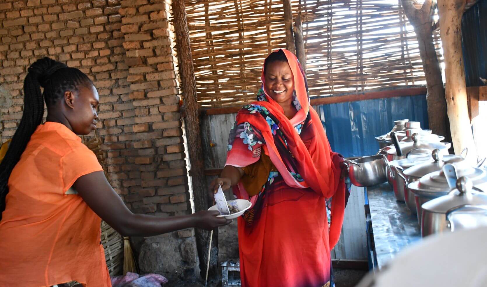 Fatuma Mahamoud serves food to a customer in a modest kitchen with brick walls and woven wooden panels.