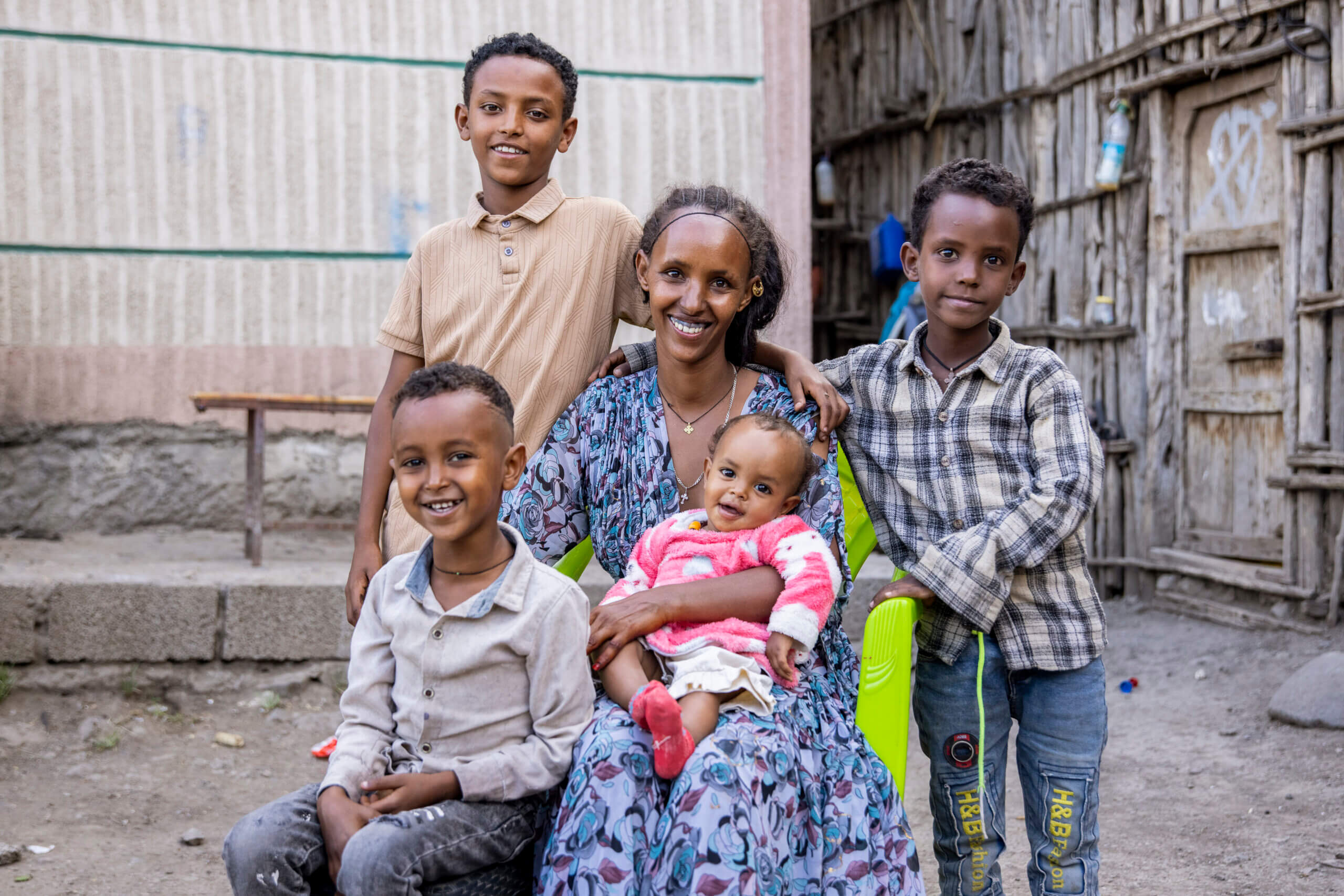 Meaza Billi and her children, (from left to right) Zecharias, Natneal, Siket and Amanuale, were treated for trachoma during a mass drug administration campaign (MDA) in Tigray, Ethiopia. Two boys stand in the back, the mother sits in a chair, with a younger boy and toddler on her lap. They are outside and are all smiling.