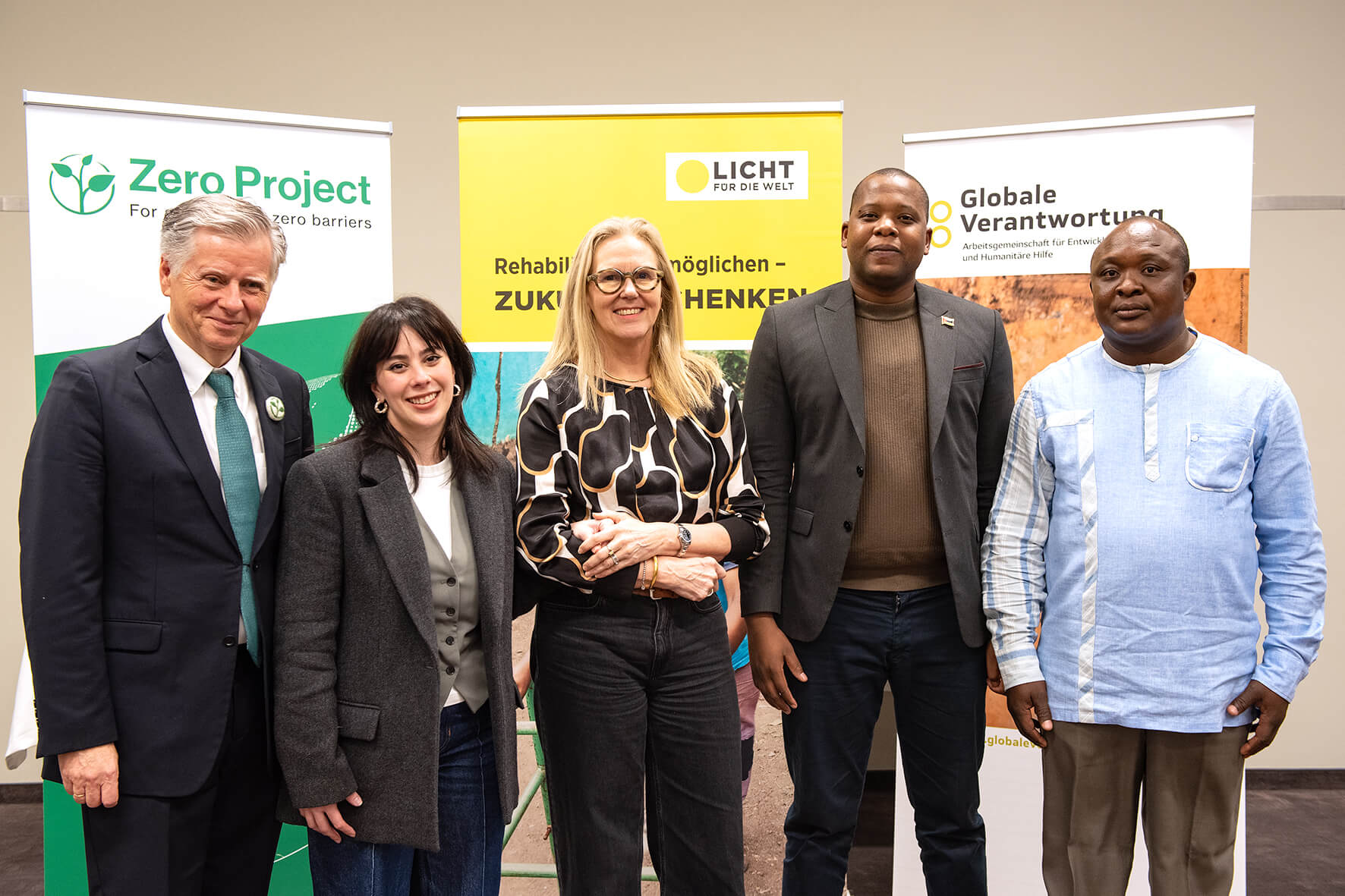 Five people stand in front of banners in a conference room, three men and two women. They are all wearing formal clothes and smiling. From left to right: Michael Fembek, CEO at Zero Project, Ioanna Tsigiridi, Innovation Manager at Elrha, Marion Lieser, CEO at Light for the World International, Clodoaldo Castiano, Executive Director at FAMOD and Ghislain Tihanibie Hien, IMPACT-BF Project Manager at Light for the World Copyright: Global Responsibility