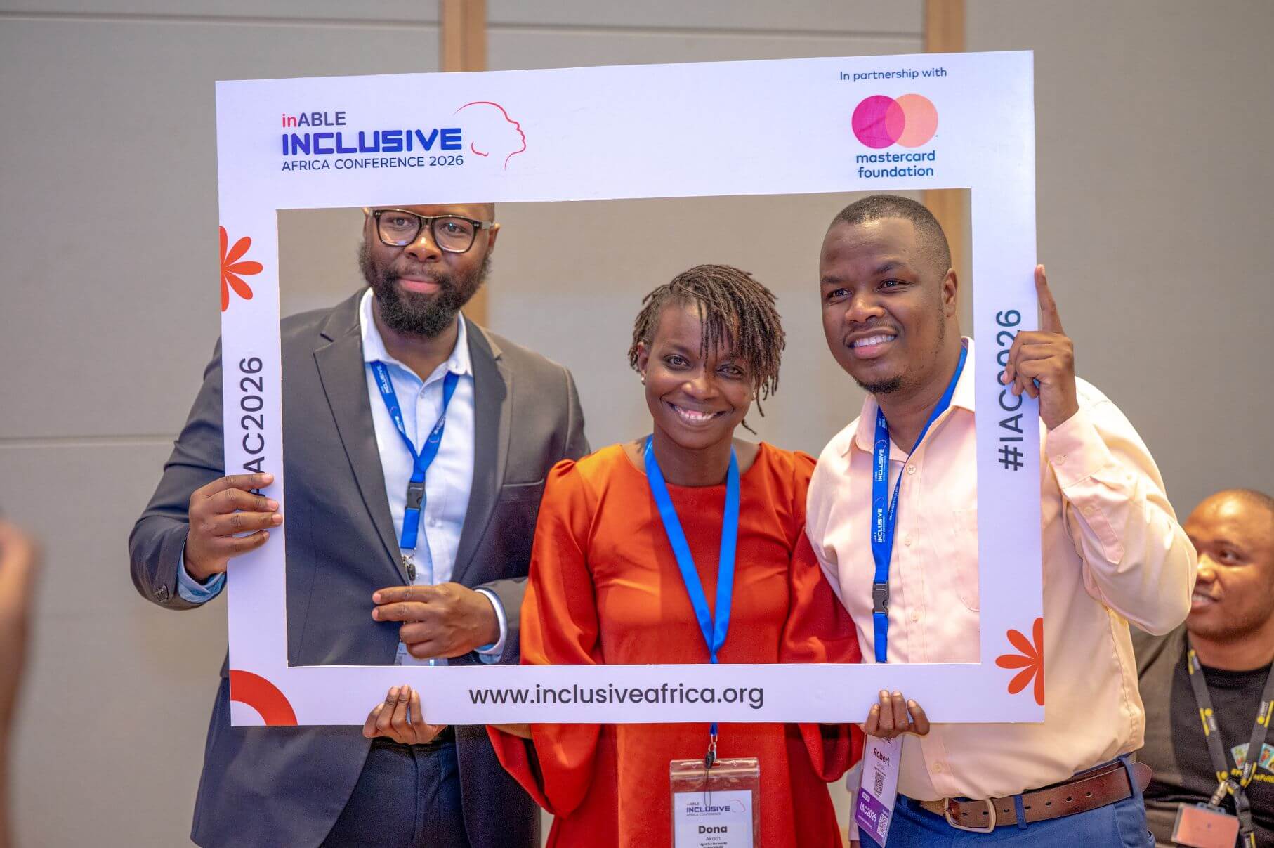Three people smile as they pose together behind an Inclusive Africa Conference 2026 photo frame at the event.