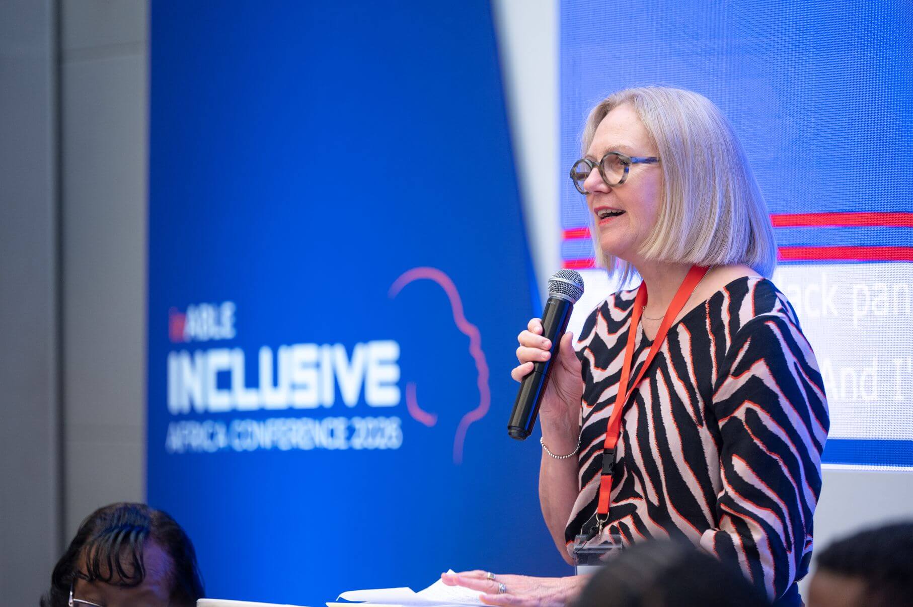 Light for the World CEO Marion Lieser speaks into a microphone at a podium, with an Inclusive Africa Conference 2026 banner behind her.