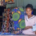 Juster Kathure Michubu smiles as she holds up a length of patterned fabric in her tailoring shop in Kenya. © MFC Production/Light for the World