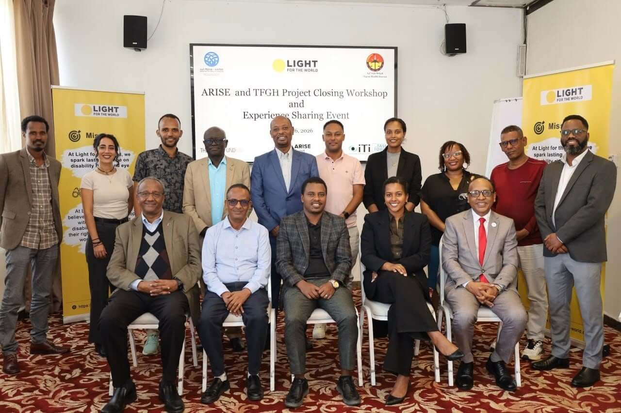 A group of workshop participants pose for a photograph in front of a screen reading "ARISE and TFGH Project Closing Workshop and Experience Sharing Event", with Light for the World banners on either side.